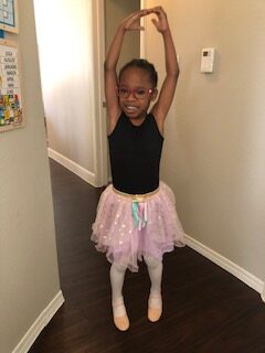 a young student ballet dancing in her living room with a big smile