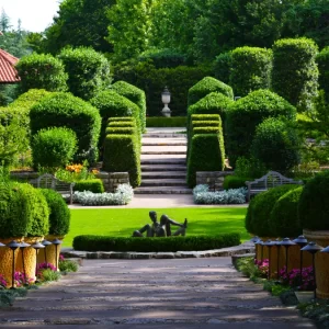 A picture of a lush and expertly manicured garden space with impressionist statues and a big gazebo.