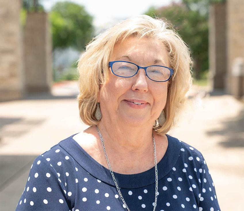 A picture of Debra Sewell standing in a lush courtyard