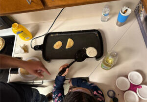 A young girl flips pancakes on a griddle at the ecc summer camp in Brownsville June 2023