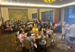 Students and teachers eat dinner in a large convention hall full of tables